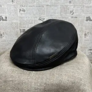 A black leather hat sitting on top of a tan blanket.